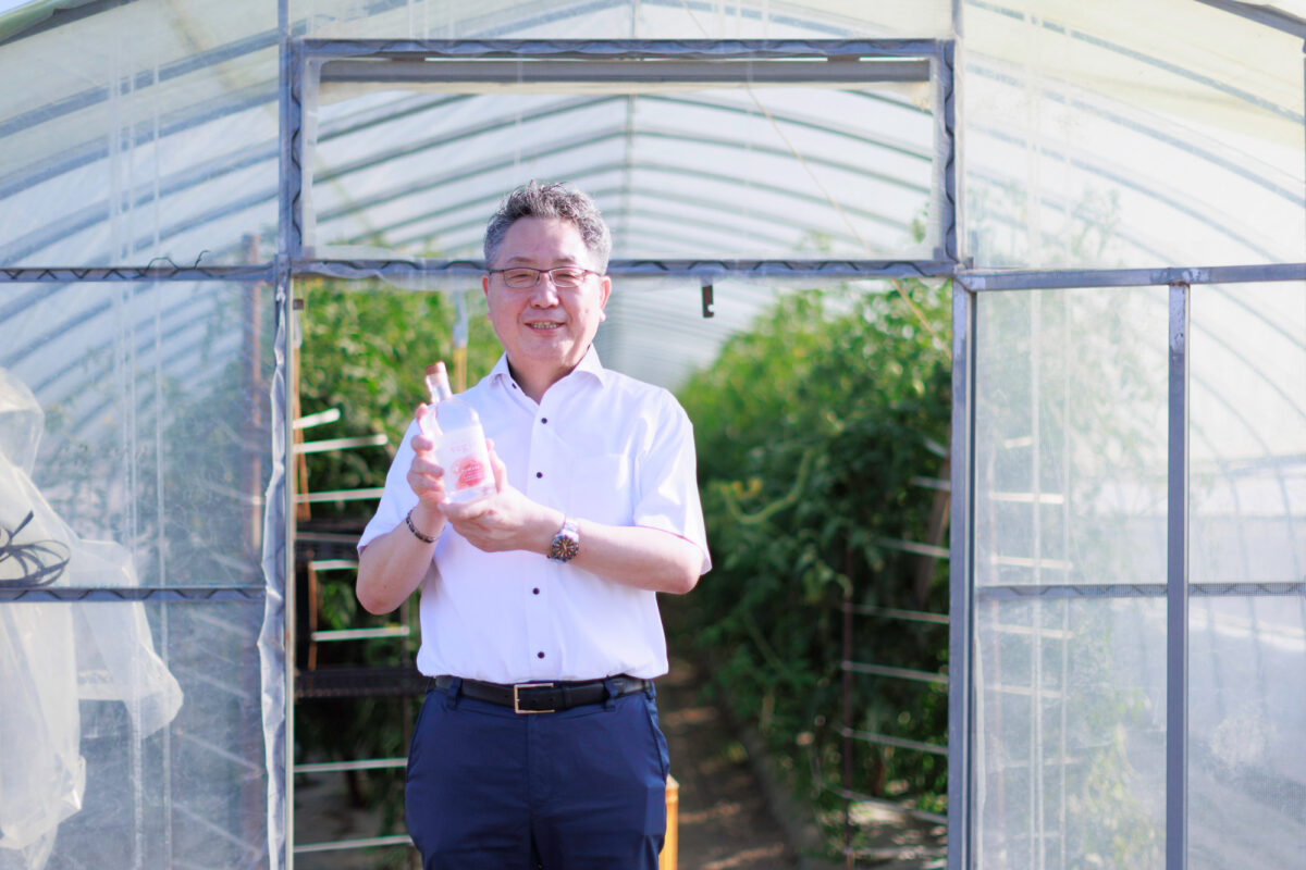 トマト圃場の前でveginをもつ波川さん